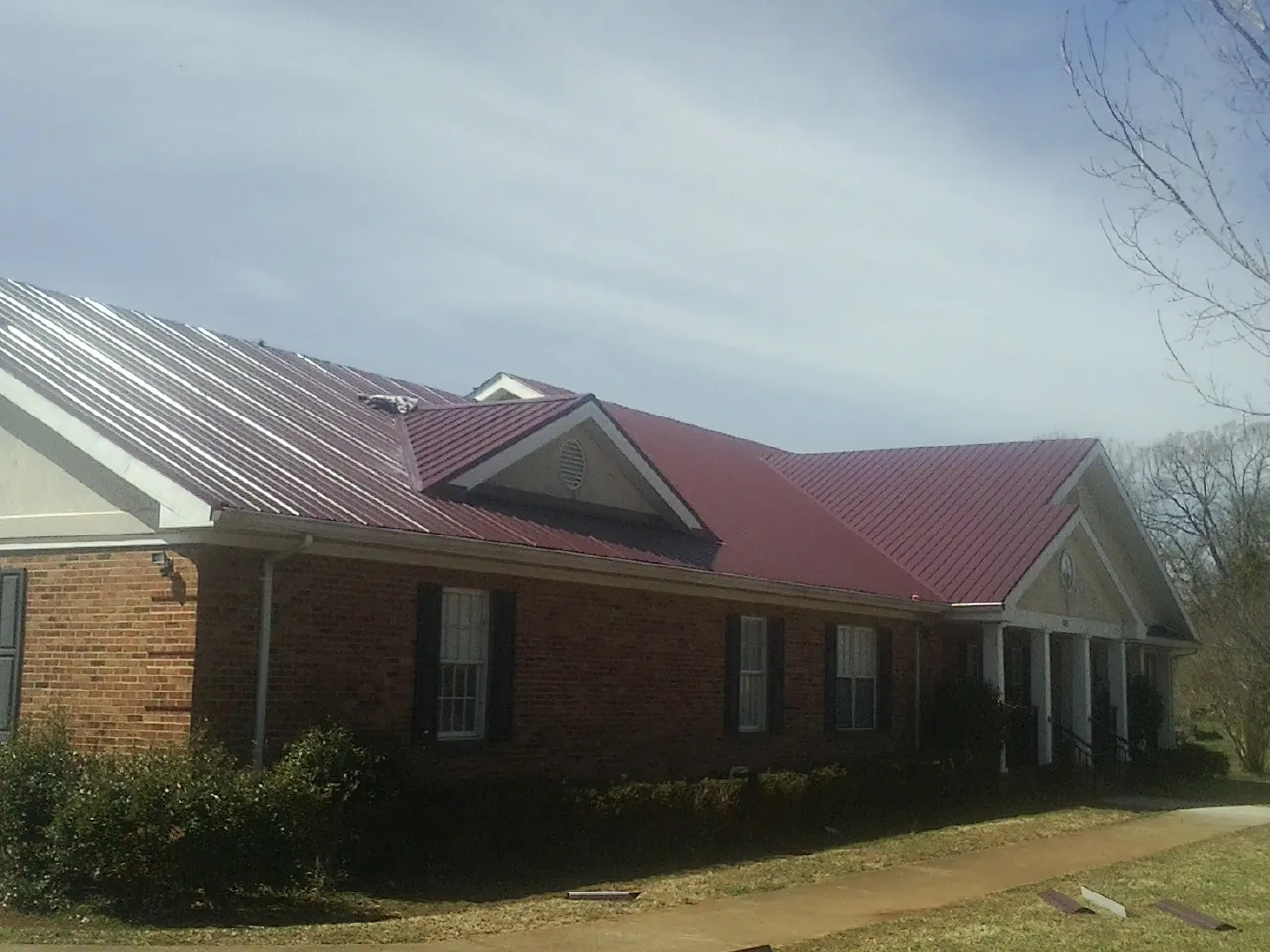 Red metal roof with gabled entries on a long brick building, from a Hail Damage Roof Repair job in Coronado