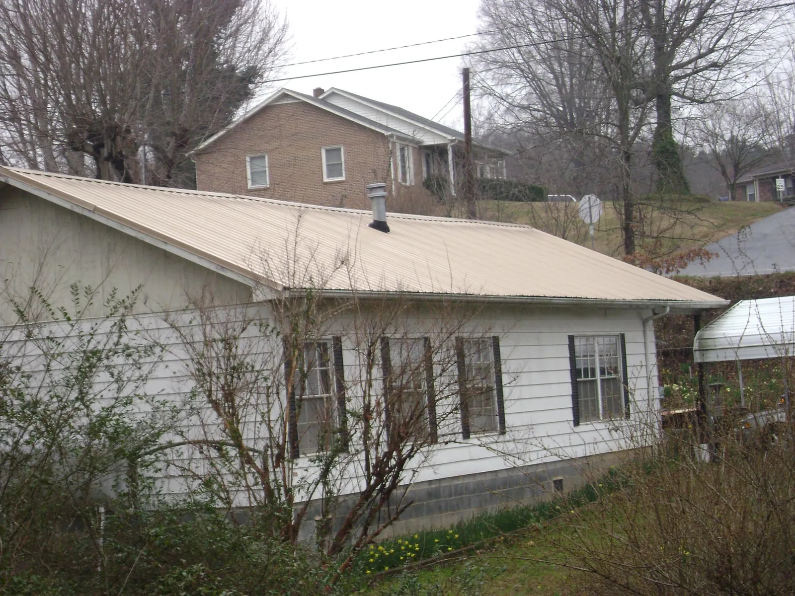 Tan metal roof on a white sided house set into a hillside — Commercial Roofing by Roofing Brothers in Coronado